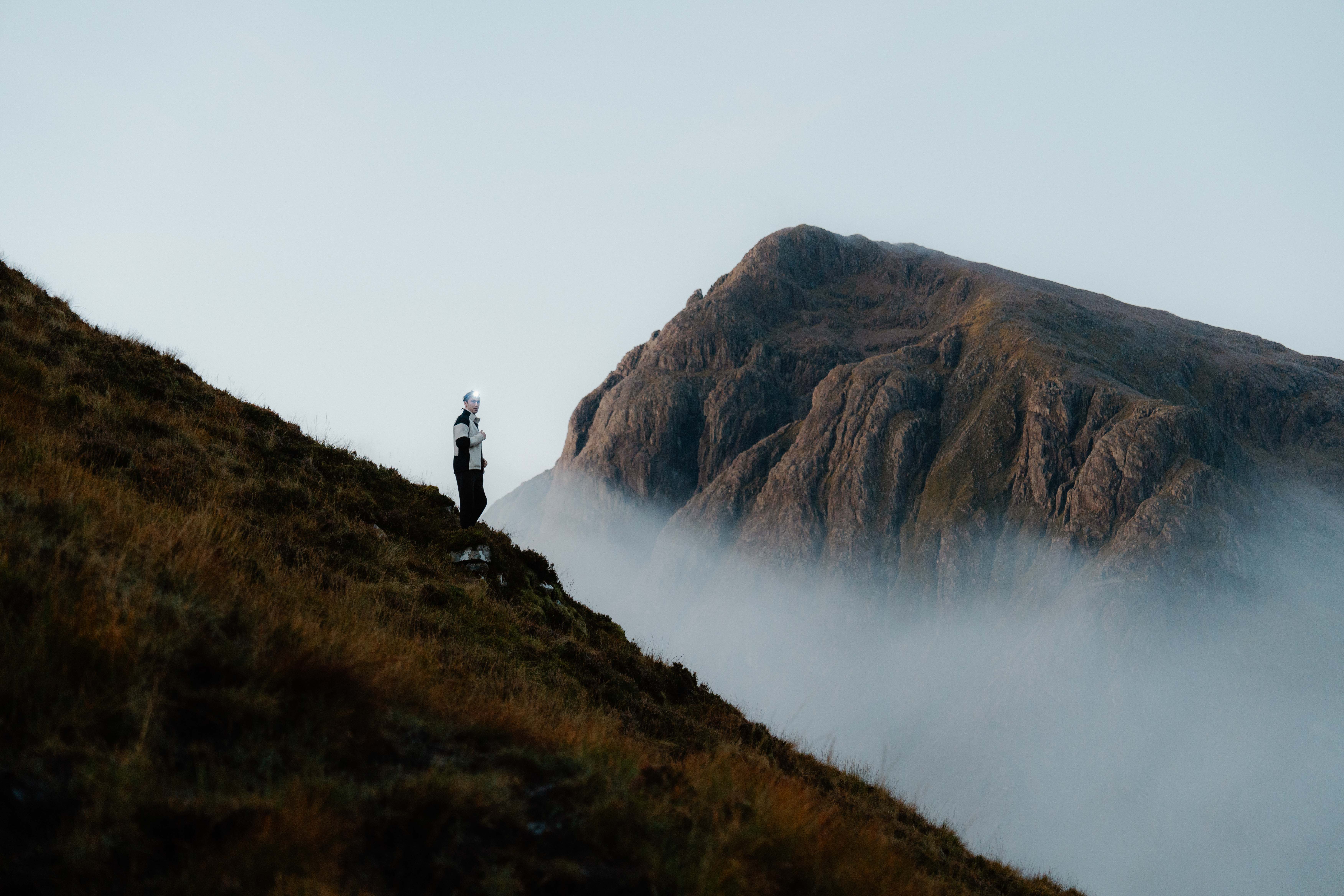 A person standing on a steep slope, with crags in the background